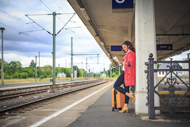 Germany, young woman at rail station in Sonneberg, reading newspaper - VTF000558