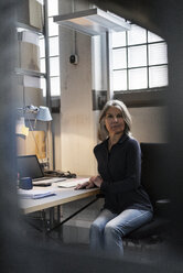 Ältere Frau sitzt am Schreibtisch in einer Fabrik - KNSF000109