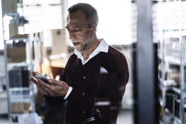 Älterer Mann in einer Fabrik, der ein Mobiltelefon benutzt - KNSF000153