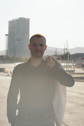 Portrait of businessman at backlight carrying jacket on his shoulder - SKCF000139