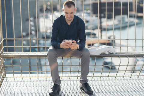 Geschäftsmann sitzt auf einer Bank vor dem Hafen und schreibt eine SMS, lizenzfreies Stockfoto