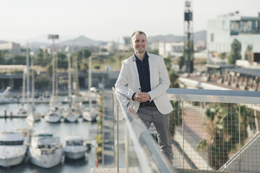 Spanien, Barcelona, lächelnder Geschäftsmann vor dem Hafen stehend - SKCF000144