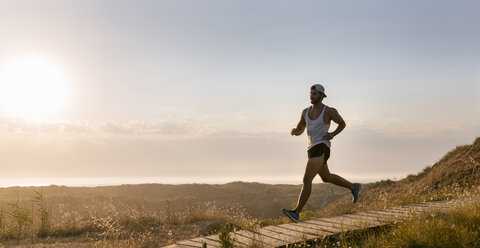 Spain, Aviles, athlete man running along a coastal path at sunset - MGOF002120