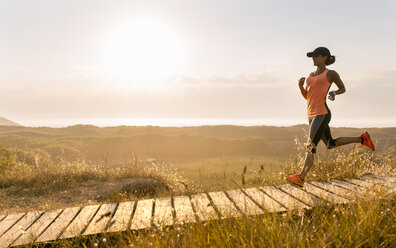 Spain, Aviles, young athlete woman running along a coastal path at sunset - MGOF002121