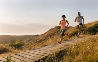 Spanien, Aviles, Sportlerpaar läuft bei Sonnenuntergang einen Küstenweg entlang - MGOF002123