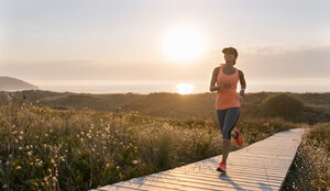 Spain, Aviles, young athlete woman running along a coastal path at sunset - MGOF002137