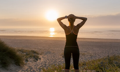 Spanien, Aviles, junge Sportlerin, die den Sonnenuntergang am Strand genießt - MGOF002140