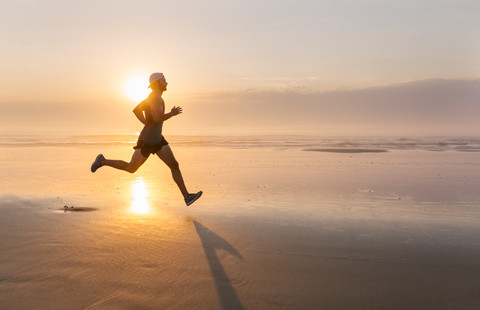 Man running on the beach at sunset stock photo