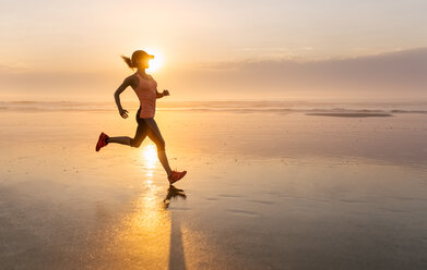 Woman running on the beach at sunset - MGOF002144