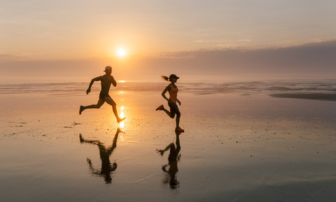 Athletenpaar beim Laufen am Strand bei Sonnenuntergang, lizenzfreies Stockfoto