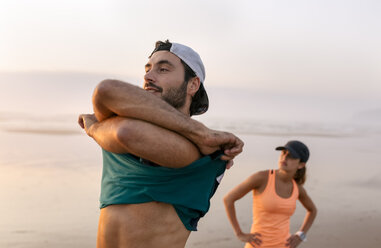 Athletes couple training on the beach in the evening, man undressing t-shirt - MGOF002147