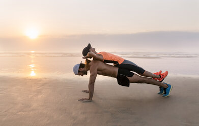 Athletenpaar beim Training am Strand bei Sonnenuntergang, Liegestütze - MGOF002148