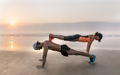 Athletenpaar beim Training am Strand bei Sonnenuntergang, Liegestütze - MGOF002149