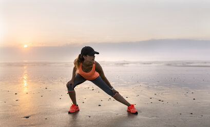 Junge sportliche Frau beim Stretching am Strand bei Sonnenuntergang - MGOF002153