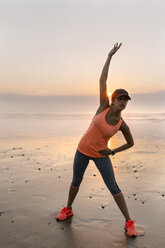 Junge sportliche Frau beim Stretching am Strand bei Sonnenuntergang - MGOF002154