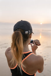 Junge Sportlerin, die am Strand bei Sonnenuntergang auf ihre Smartwatch schaut - MGOF002156