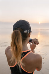 Young athlete woman looking the smartwatch on the beach at sunset - MGOF002156