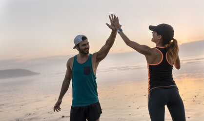 Sportlerpaar bei Sonnenuntergang am Strand im Fünferpack - MGOF002157