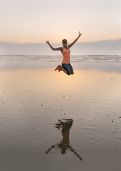 Junge Sportlerin, die abends am Strand springt - MGOF002158