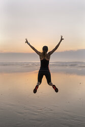 Junge Athletin, die bei Sonnenuntergang am Strand springt - MGOF002159