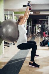 Pregnant woman doing exercises with hand handles and fitness ball in gym - ZEDF000266