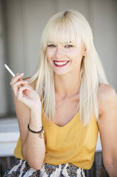 Portrait of smiling blond woman smoking cigarette - GDF001094