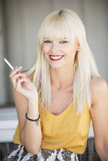 Porträt einer lächelnden blonden Frau, die eine Zigarette raucht - GDF001094