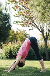 Junge Frau übt Yoga im Park, Downward Facing Dog Position - BZF000328