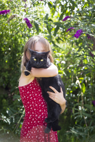 Little girl standing in garden with black cat on her arms stock photo