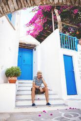 Griechenland, Insel Amorgos, junger Mann, der auf einer Stufe sitzt und mit einem Handy telefoniert - GEMF000945