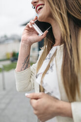 Glückliche Frau mit Tattoo auf dem Arm am Mobiltelefon - DAPF000220