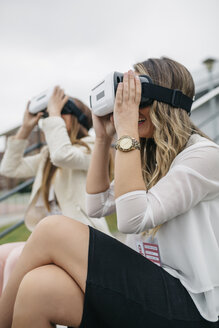 Zwei Frauen haben Spaß mit VR-Brille im Freien sitzend - DAPF000238
