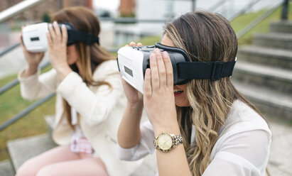 Two women having fun with VR glasses sitting outdoors - DAPF000239