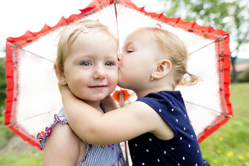 Little girl kissing her sister under an umbrella - HAPF000688