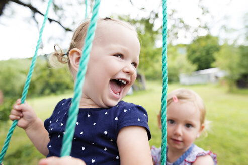 Laughing little girl on a swing with sister in the background - HAPF000689