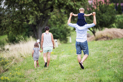 Rückenansicht einer Familie mit zwei Kindern beim Spaziergang auf einer Wiese - HAPF000700