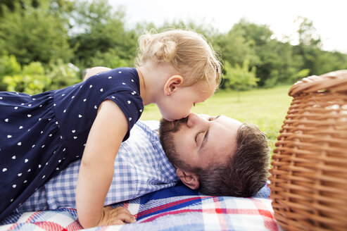 Little girl kissing her father lying on blanket on a meadow - HAPF000704