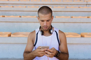 Junger Sportler mit Kopfhörern und Smartphone - FMOF000068