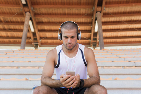 Junger Sportler mit Kopfhörern und Smartphone - FMOF000070