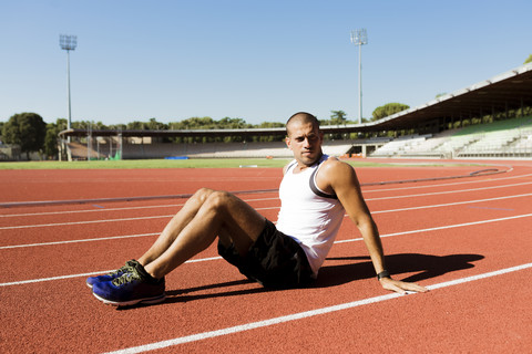 Young sportsman sitting on running track stock photo