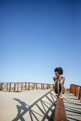 Junge Frau sitzt auf dem Geländer eines Stegs am Strand - KIJF000654