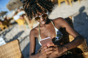 Junge Frau benutzt ein Smartphone in einer Strandbar - KIJF000662