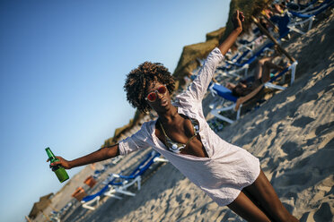 Junge Frau tanzt am Strand mit einem Bier in der Hand - KIJF000673