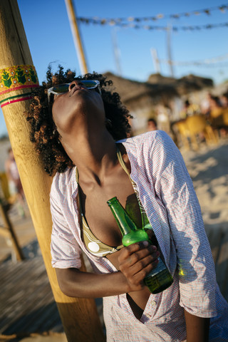 Junge Frau am Strand entspannt mit einer Flasche Bier, lizenzfreies Stockfoto