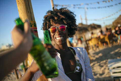 Junge Frau am Strand stößt mit einer Bierflasche an, lizenzfreies Stockfoto