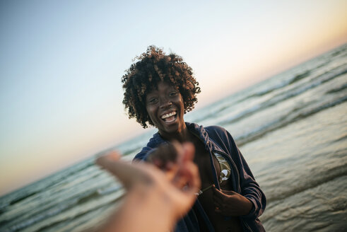 Junge Frau nimmt Hand eines Mannes am Strand bei Sonnenuntergang - KIJF000687