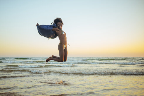 Junge Frau springt bei Sonnenuntergang am Strand - KIJF000689