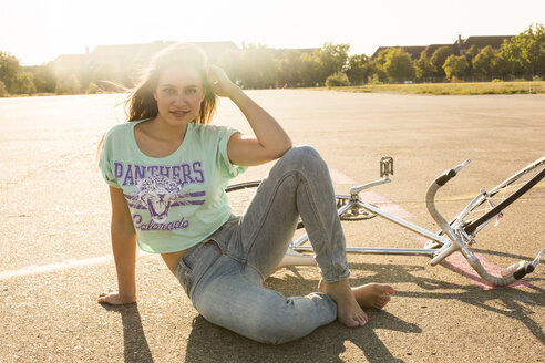 Lächelnde junge Frau mit Fahrrad im Gegenlicht sitzend - TKF000458