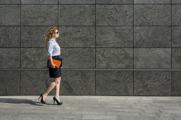 Businesswoman holding book and digital tablet walking outdoors - MAUF000681