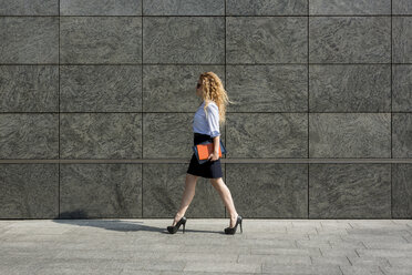 Businesswoman holding book and digital tablet walking outdoors - MAUF000682